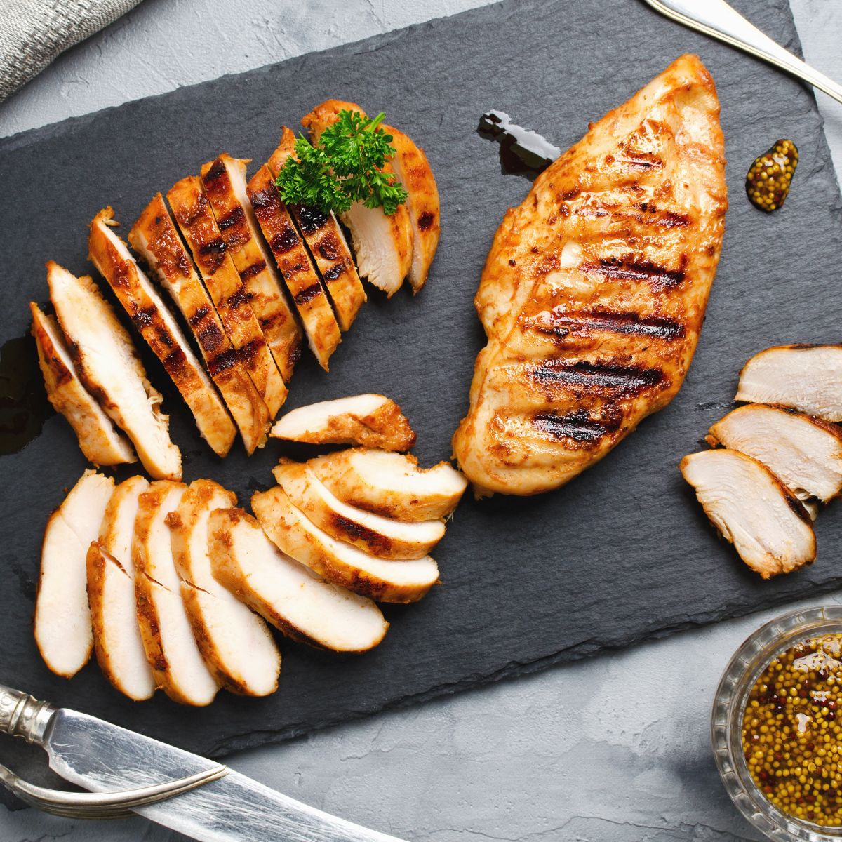 sliced chicken, mustard and utensils on slate serving board
