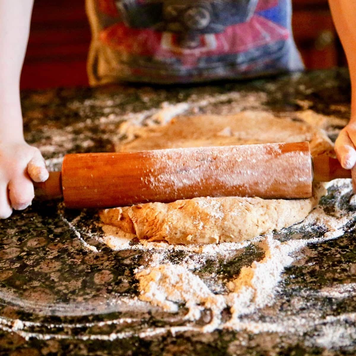child rolling out pizza dough on surface covered in flour 