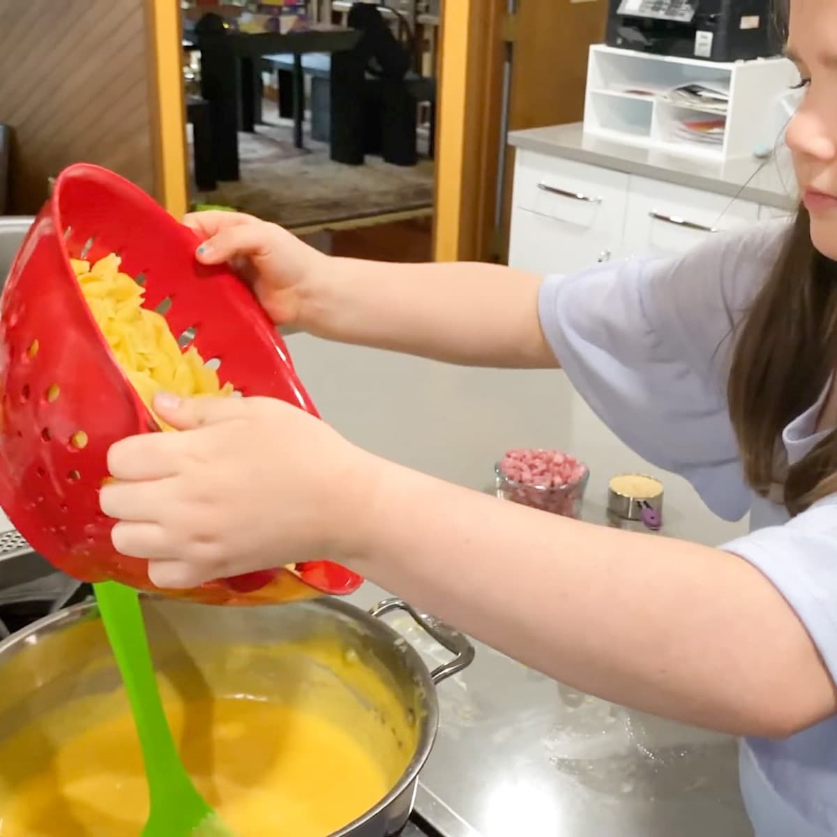 child pouring shell pasta into pot of cheese sauce
