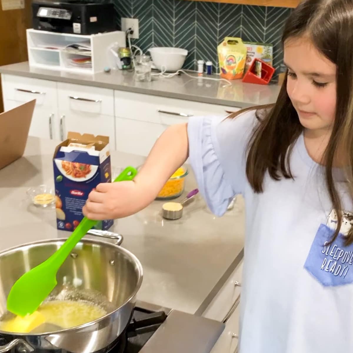 child stirring butter in pot with green spatula
