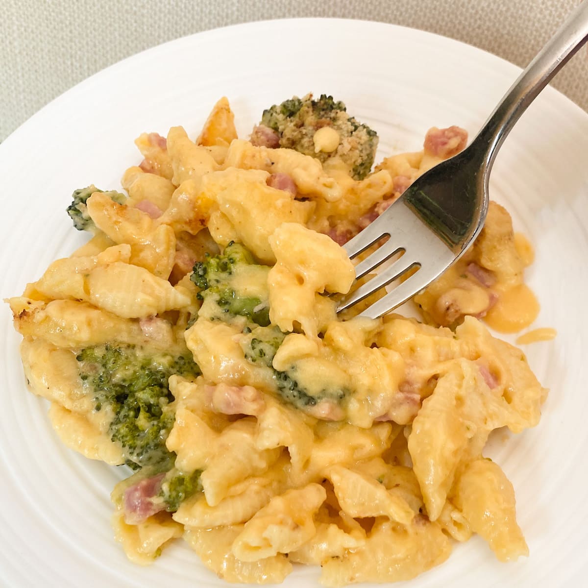 white plate of mac and cheese with ham and broccoli