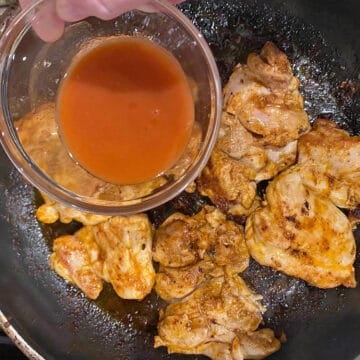 Adding a small bowl of hot sauce to cooked buffalo chicken thighs in pan. 