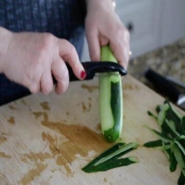 hands peeling cucumber with peeler 