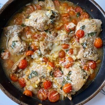 Chicken thighs topped with pomodoro sauce in black pan.