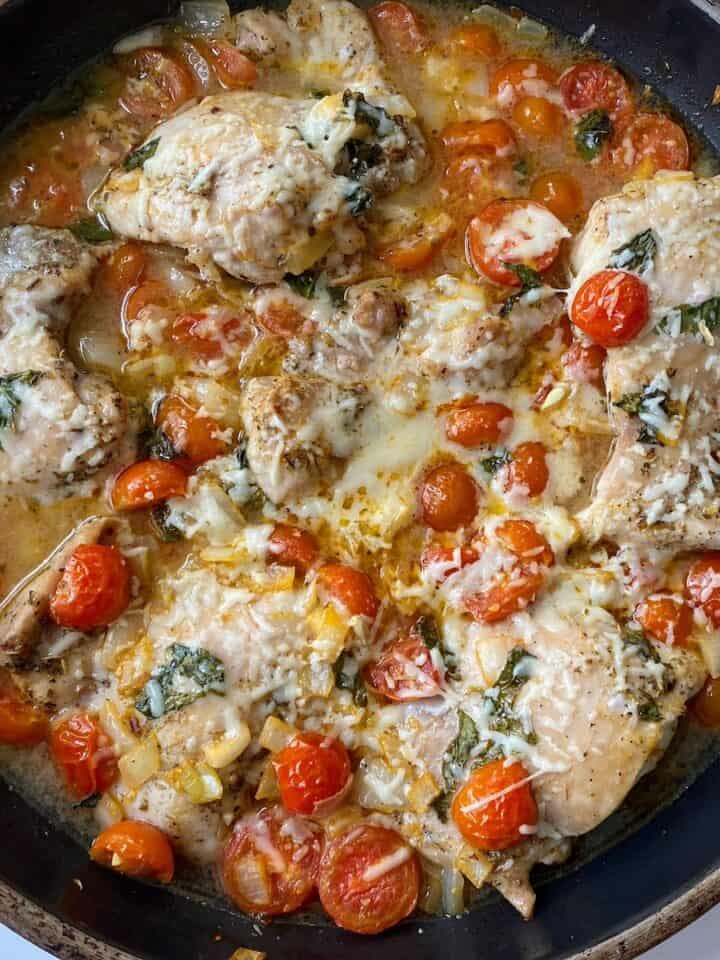 Chicken thighs topped with pomodoro sauce in black pan.