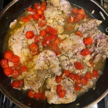 Chicken thighs in pan with tomatoes, onion and chicken broth. 