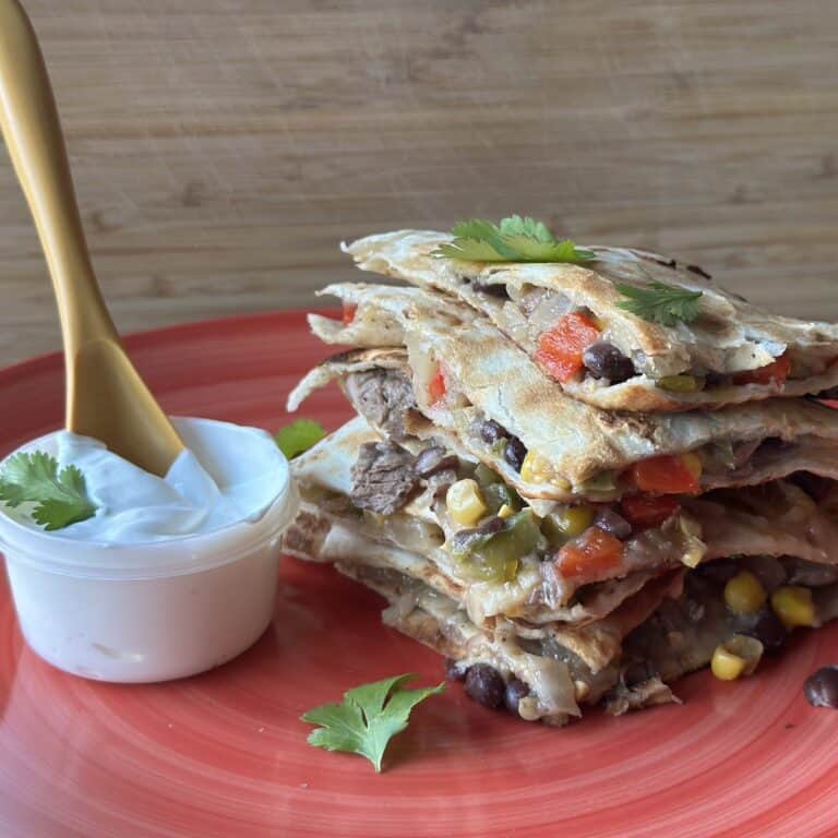 Stacked steak quesadillas served on a pink plate with a side of sour cream.