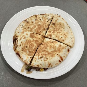 A whole steak quesadilla cooked and sliced into four pieces on a white plate.