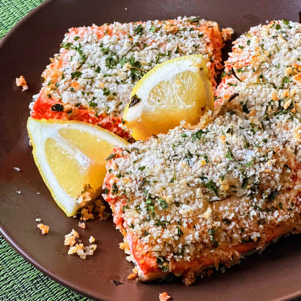 fillets of salmon with panko crust and lemon wedges on brown plate on green placemat
