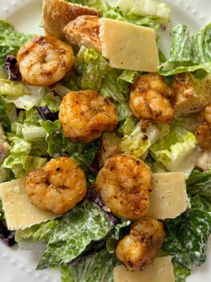 Blackened shrimp caesar salad served on a white plate and topped with parmesan cheese.