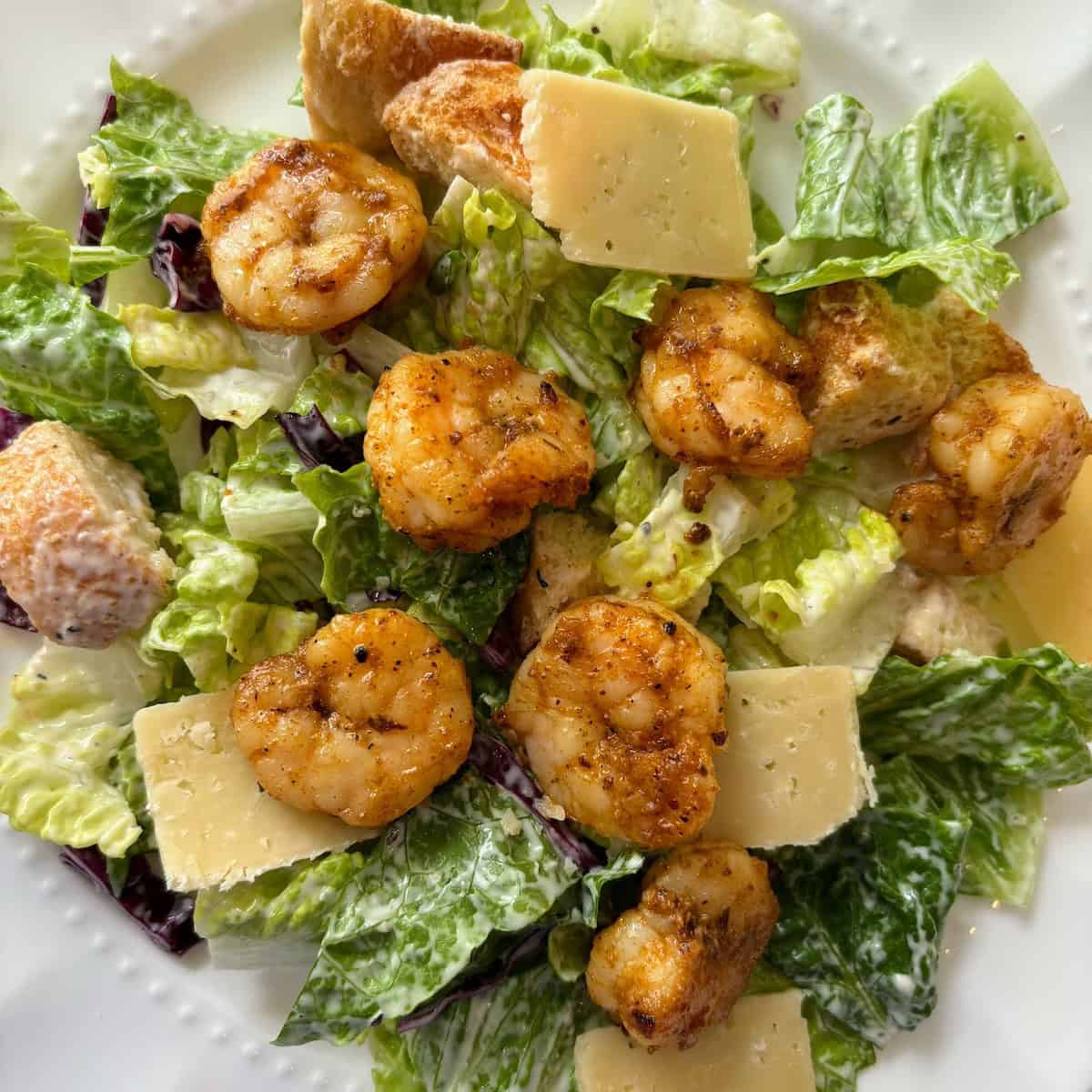 Blackened shrimp caesar salad topped with cheese on a white plate. 