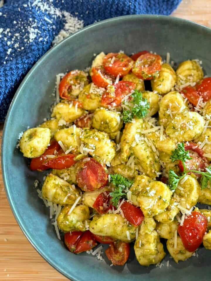 green bowl of gnocchi pasta with roasted tomatoes parsley and shredded parm