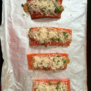 A baking sheet lined with foil and holding four salmon filets with honey mustard and panko breadcrumbs.