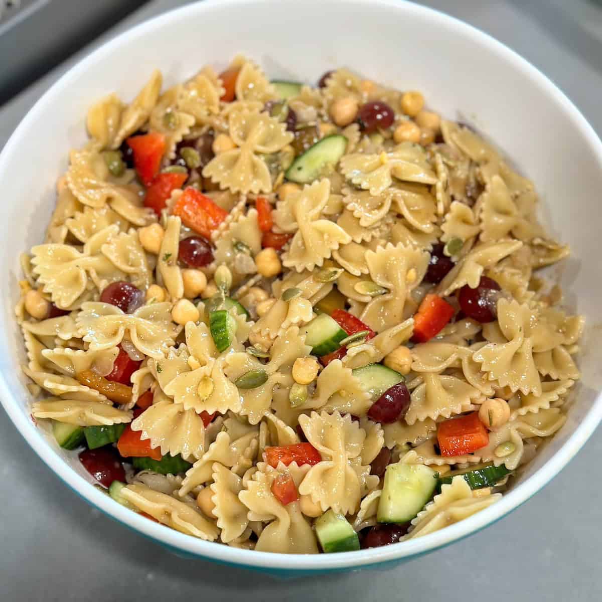 white bowl of bowtie pasta with chopped veggies tossed in a light vinaigrette