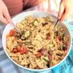 child serving up bowl of bowtie pasta salad with chopped veggies