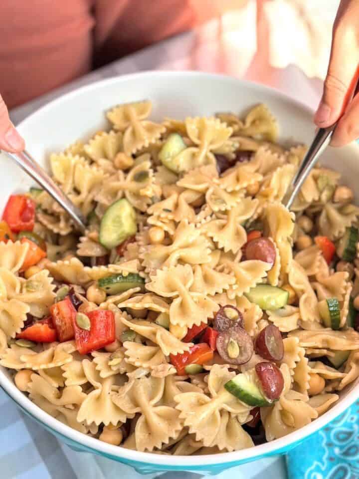 child serving up bowl of bowtie pasta salad with chopped veggies
