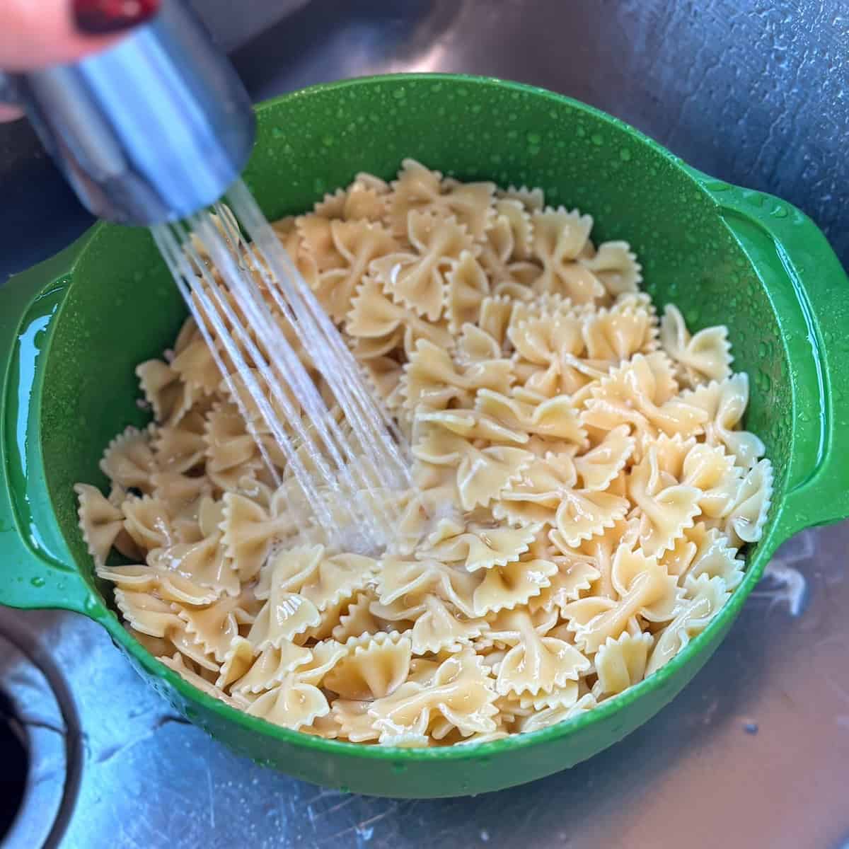 green colander filled with bowtie pasta being washed in sink
