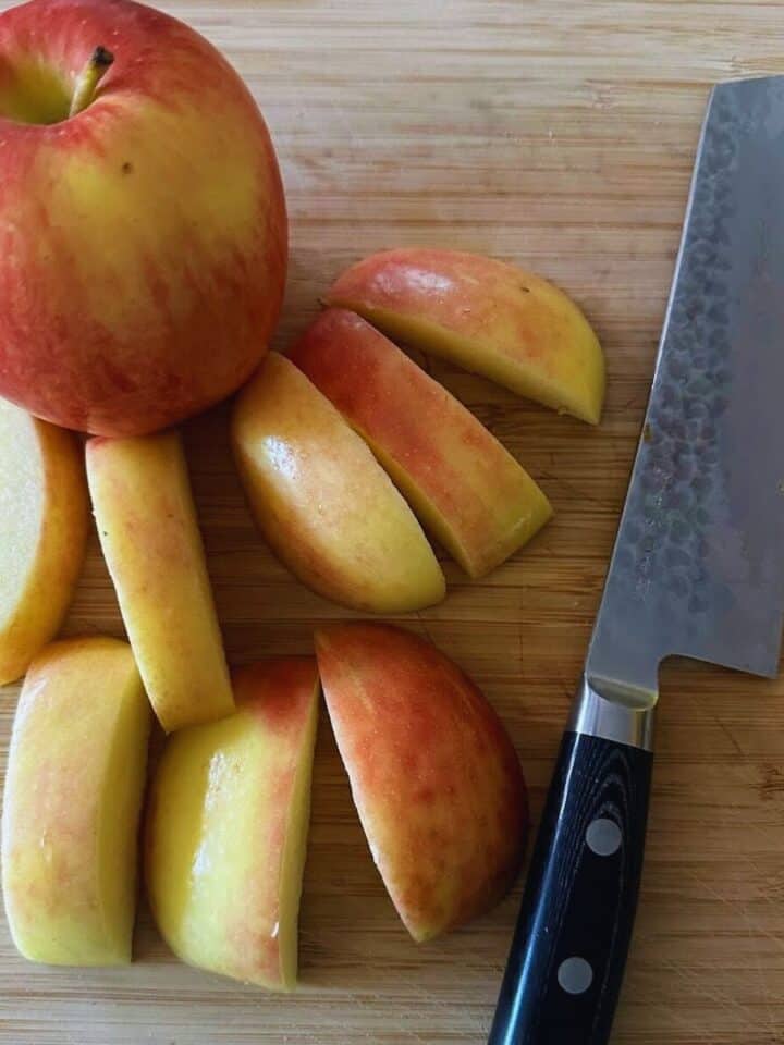 Sliced apples and whole apple on cutting board with knife.