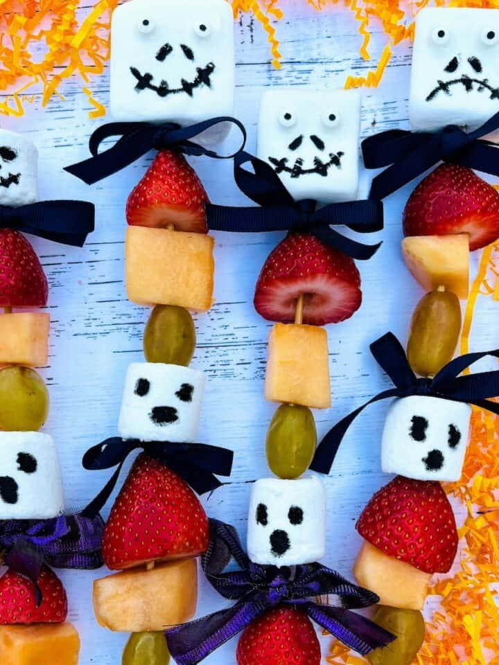 Four Halloween kabobs with ghost marshmallows and strawberries, melon and grapes.