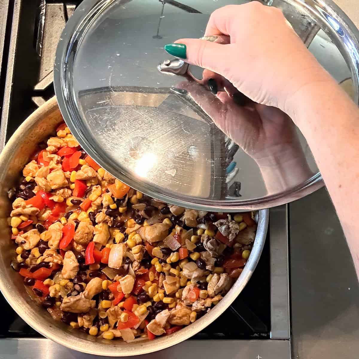 lid going on pan of chicken, beans, corn and red bell pepper