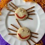 Two spider sandwiches made from peanut and butter sandwiches, pretzels and candy on a white plate.