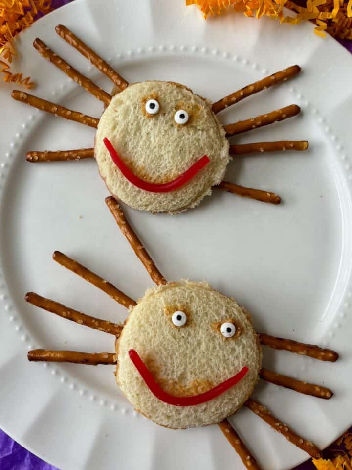 Two spider sandwiches made from peanut and butter sandwiches, pretzels and candy on a white plate.