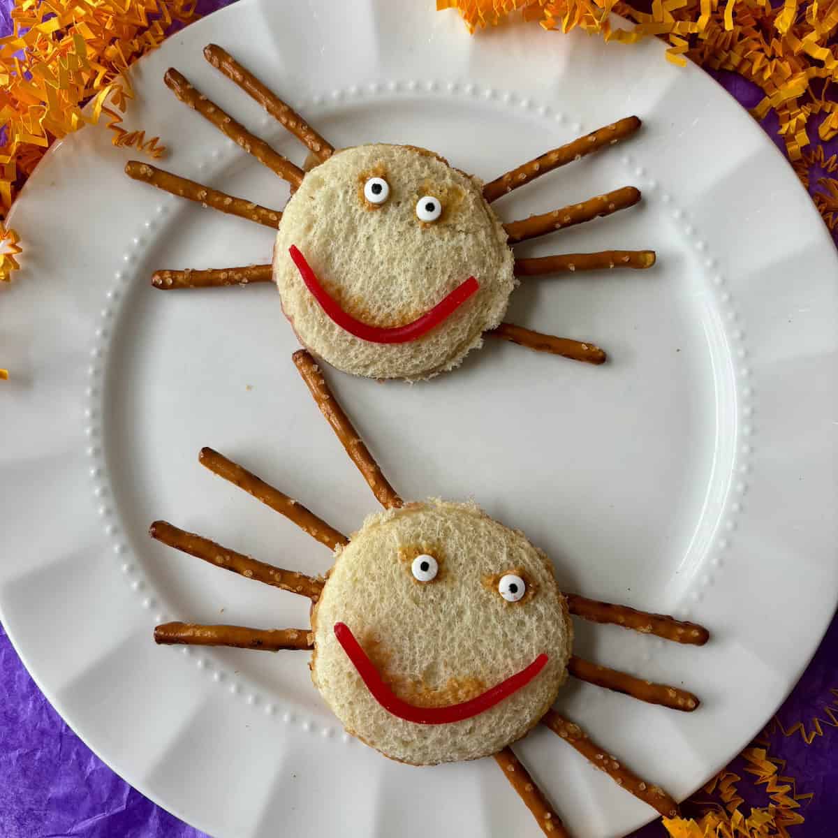 Two spider sandwiches  made from peanut and butter sandwiches, pretzels and candy on a white plate.