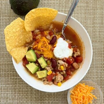 Taco soup bowl with toppings and side of cheese and an avocado.