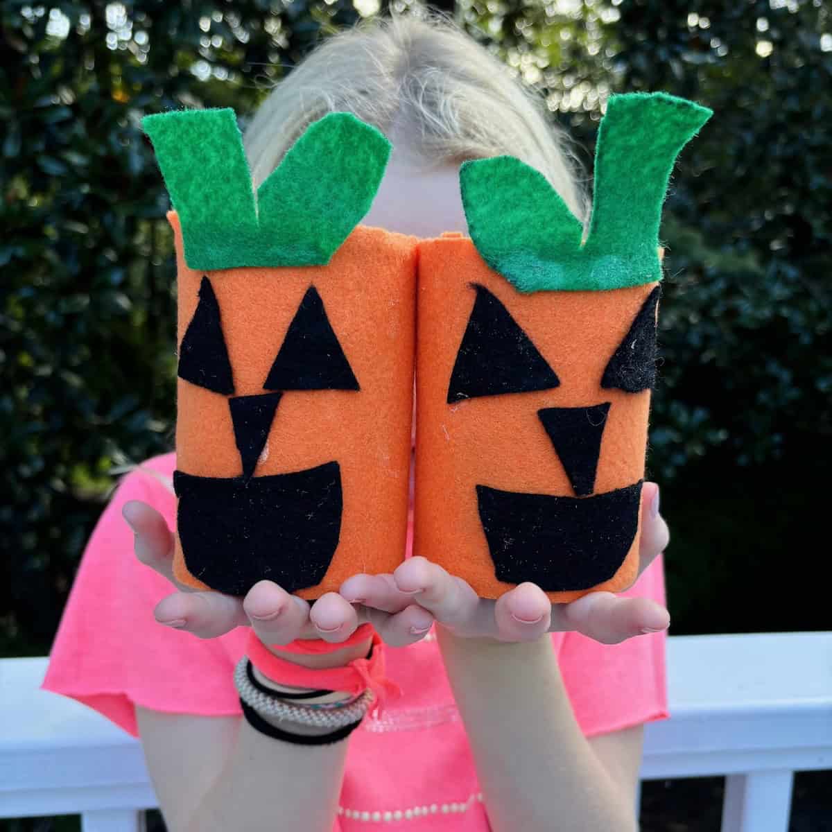 Child holding two jack-o-lanterns made from decorated empty tin cans. 