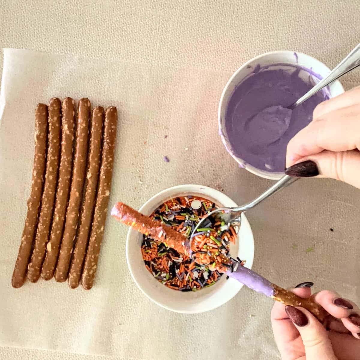 adding Halloween sprinkles to a purple candy coated pretzel rod