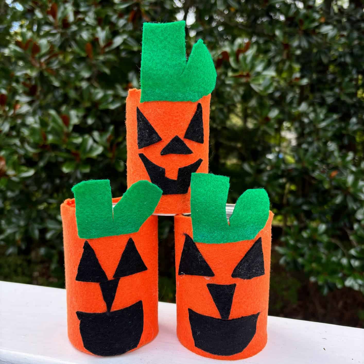 Three jack-o-lanterns stacked and made from tin cans with colored felt for Halloween. 