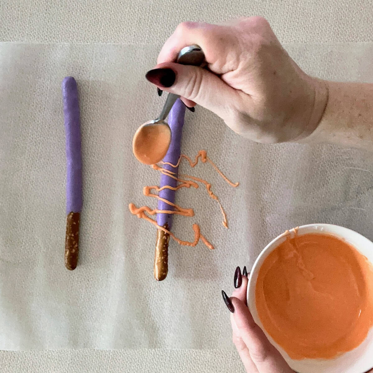 drizzling orange candy melts with a spoon onto a purple coated pretzel