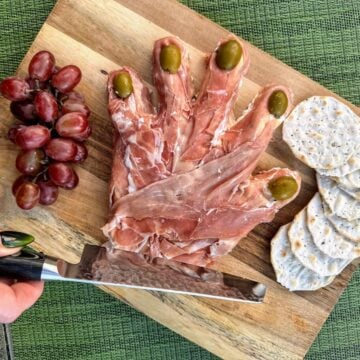 severed prosciutto hand on cutting board with grapes and sharp knife