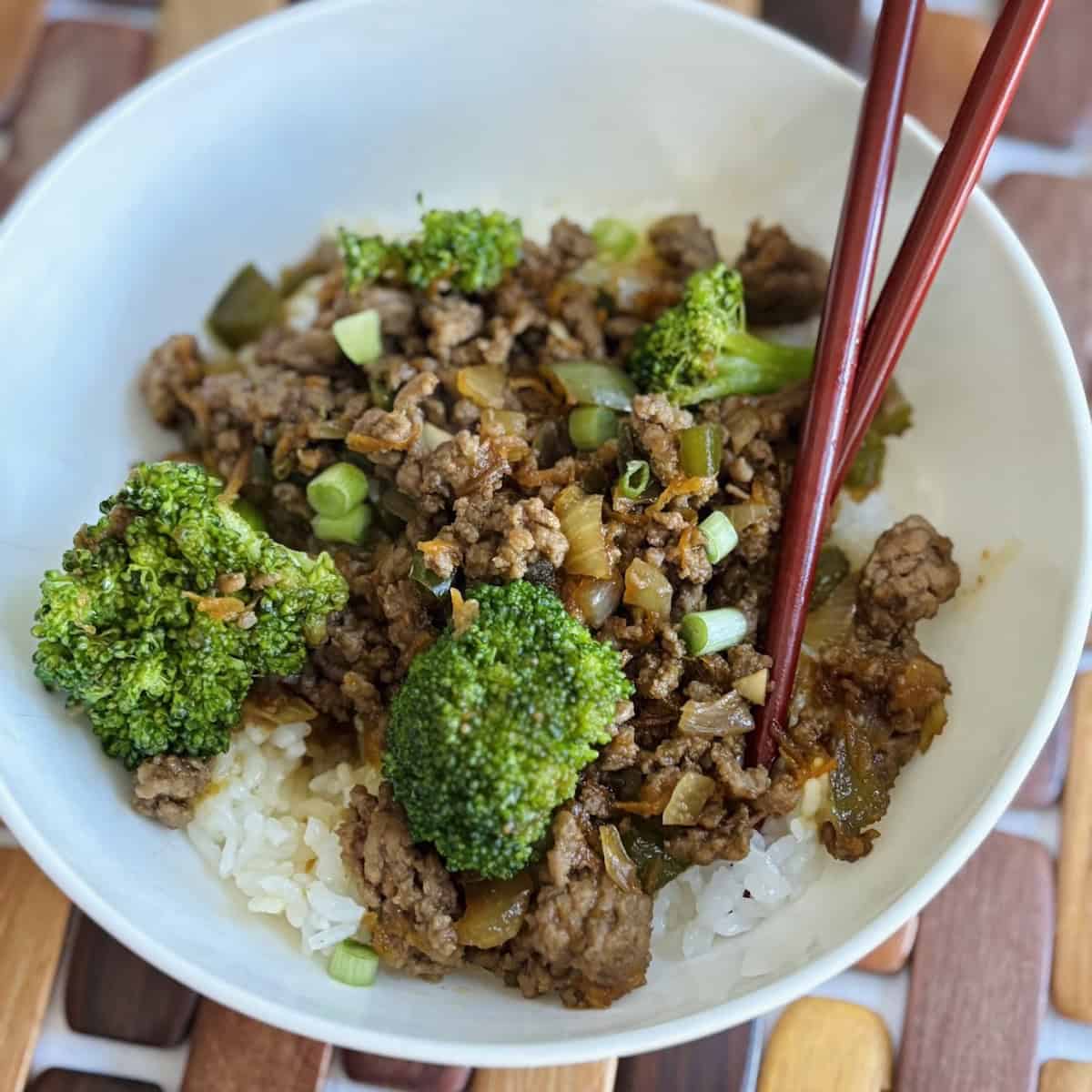 Beef teriyaki rice bowl on brown wooden placemat.