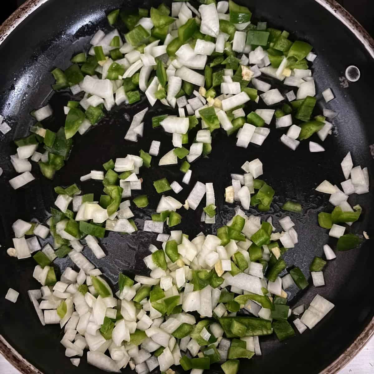 Onions, garlic and bell pepper cooking in pan in oil.