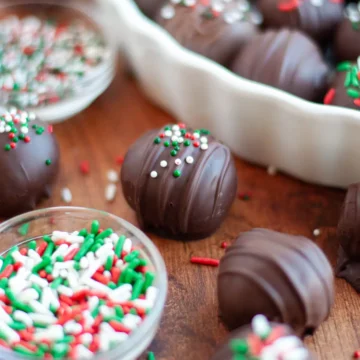 Oreo cookie balls on a bowl cutting board with a side of sprinkles.