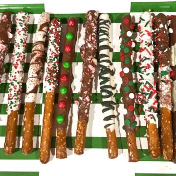 pretzels rods decorated with christmas themed sprinkles and laid vertically on green and white tray