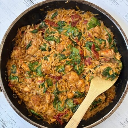 chicken orzo bake with a wooden spoon in a pan.