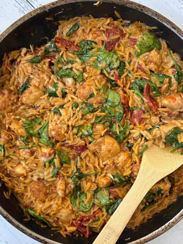 chicken orzo bake with a wooden spoon in a pan.