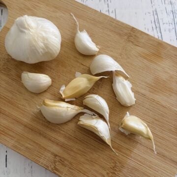 Gallic head and garlic cloves on wooden cutting board.