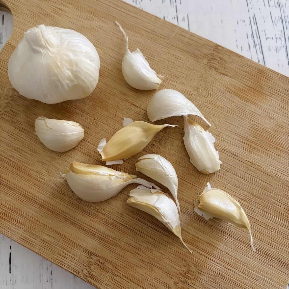 Garlic cloves and a head of garlic on a wooden cutting baord. 