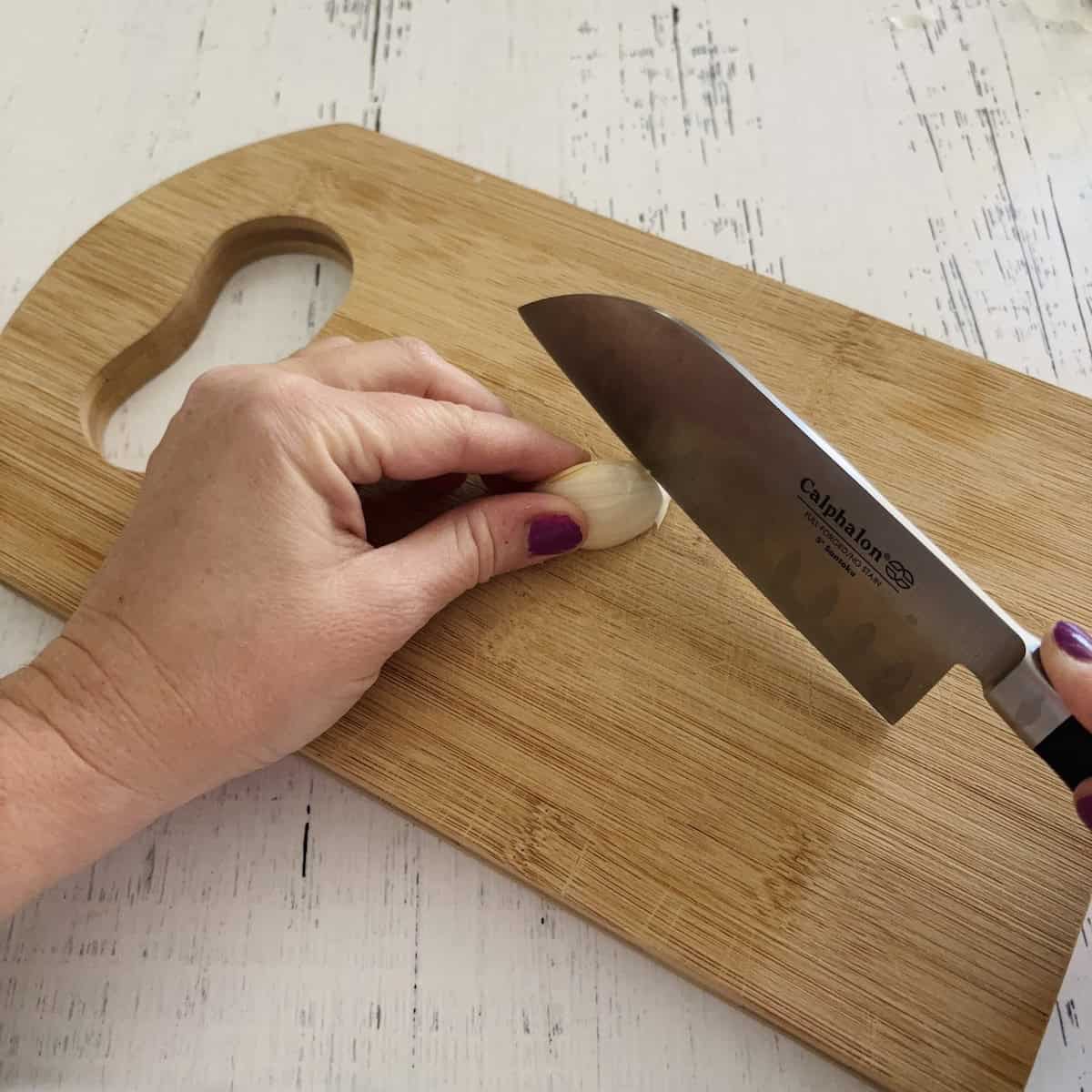 Cutting off the end of a garlic clove with a chef's knife on a wooden cutting board. 