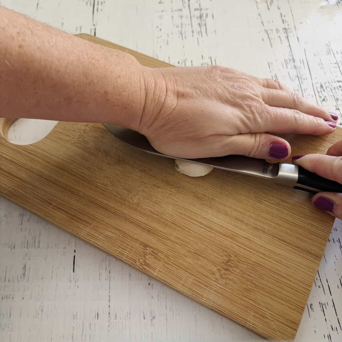 Smashing the garlic clove with the flat side of the knife using the palm of  a hand. 