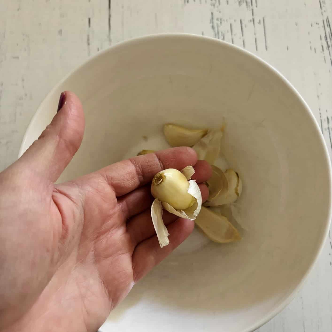 Garlic clove in a person's hand pulling away from its skin after using the microwave method. 