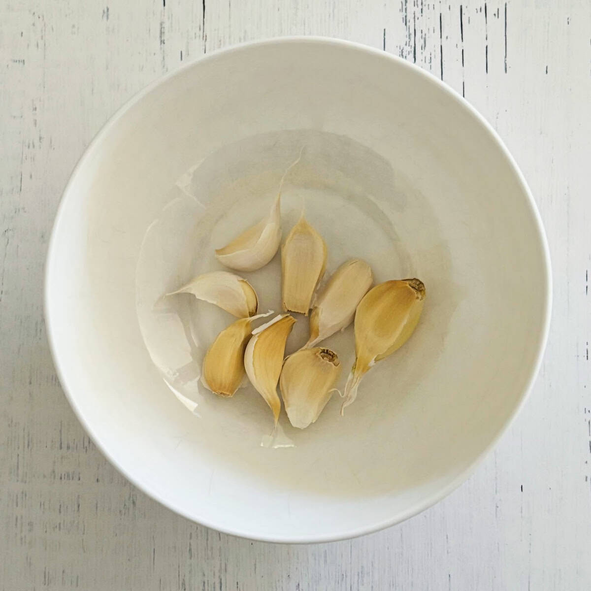 White bowl filled with 8 garlic cloves. 