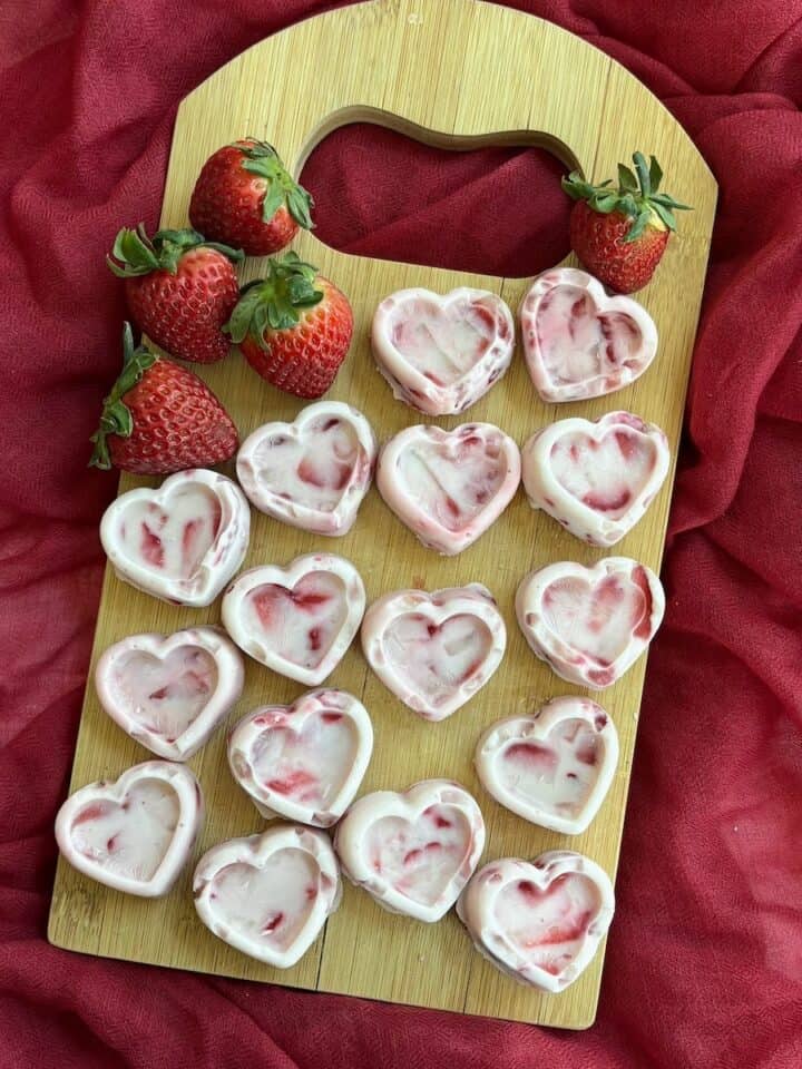 Several heart-shaped yogurt and strawberry bites on a cutting board.