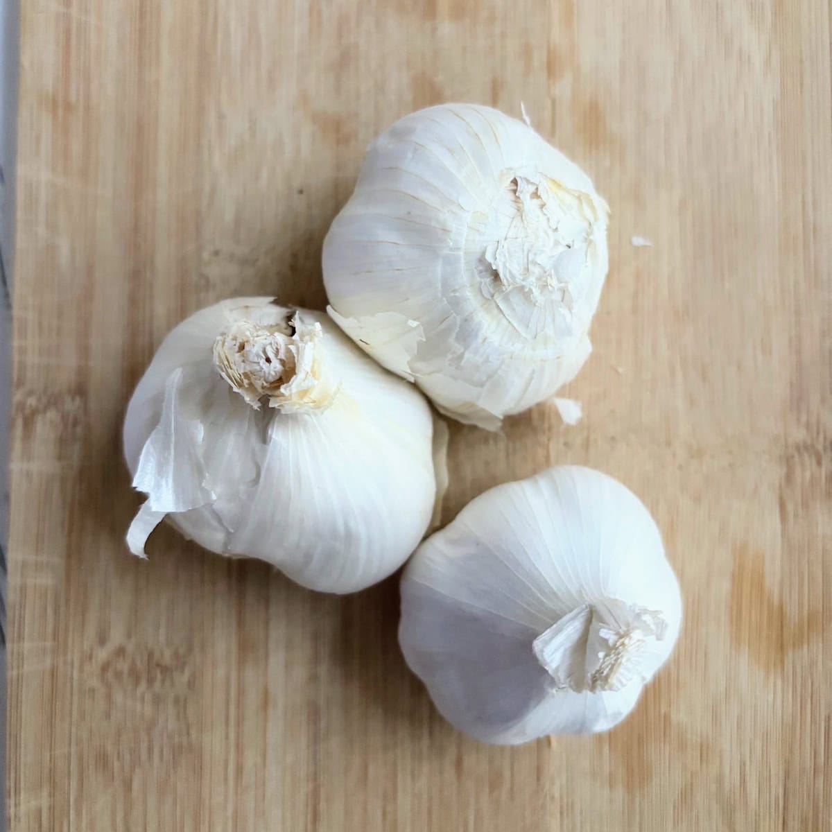 Three heads of garlic on a wooden cutting board. 