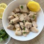 White bowl with garlic pork bites and lemon on top.