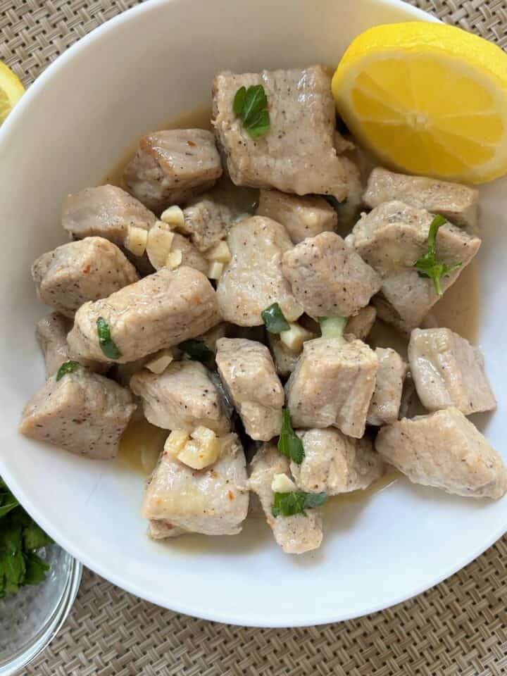 White bowl with garlic pork bites and lemon on top.