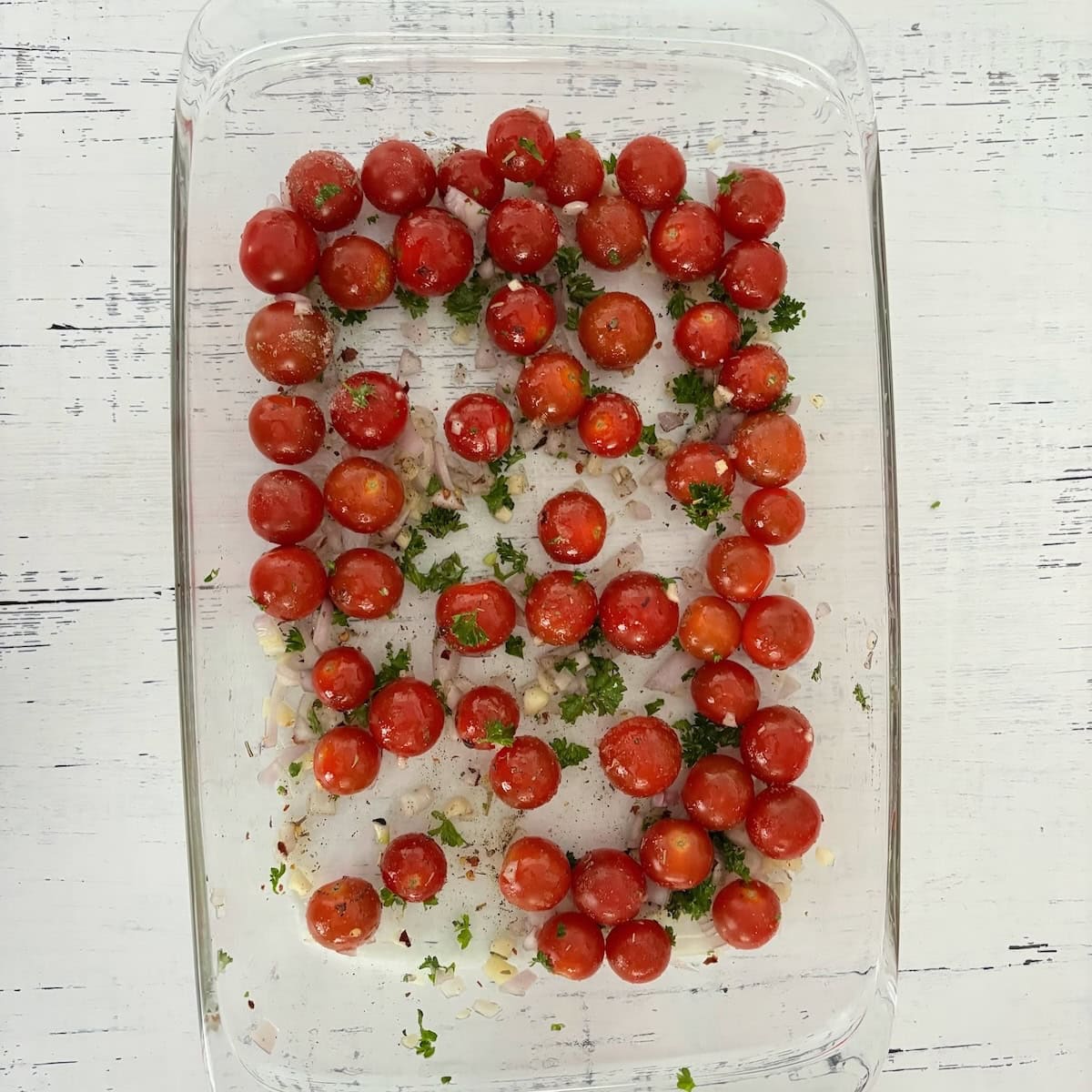 Cherry tomatoes with seasoning and parsley in a casserole dish. 